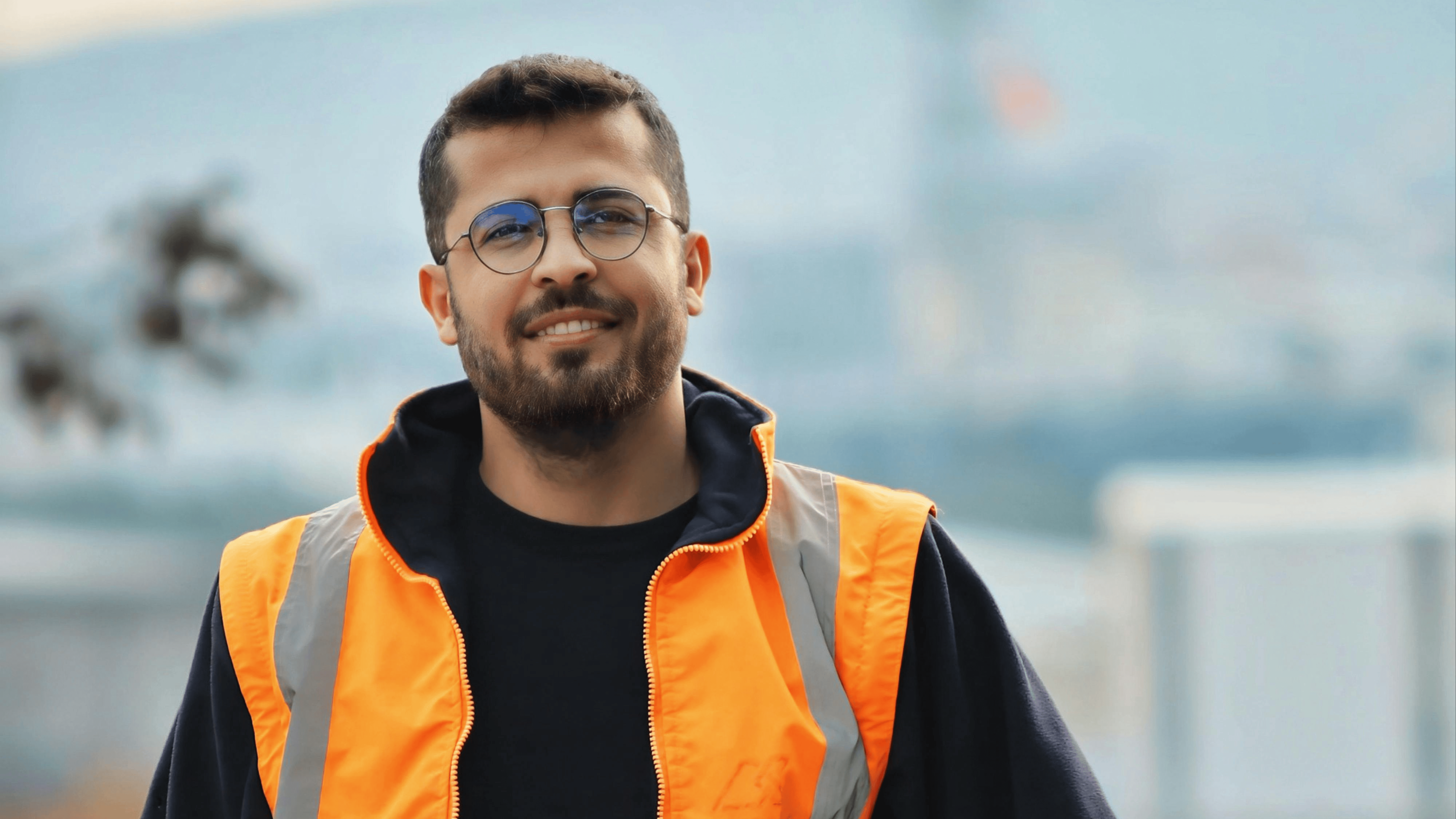 Young male construction worker in orange hi-vis vest smiling on a job site, representing casual employment in the Australian construction industry.
