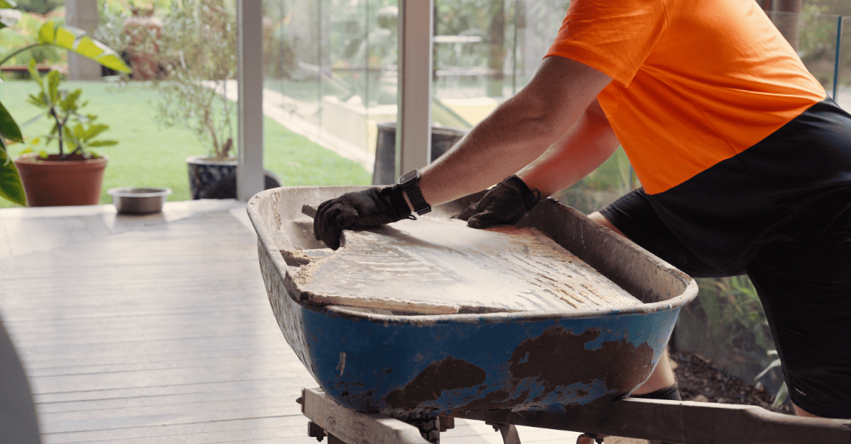 Tradesperson in high-vis workwear mixing render in a wheelbarrow on a residential construction site, representing the casual construction labour Brisbane businesses rely on to keep projects moving.