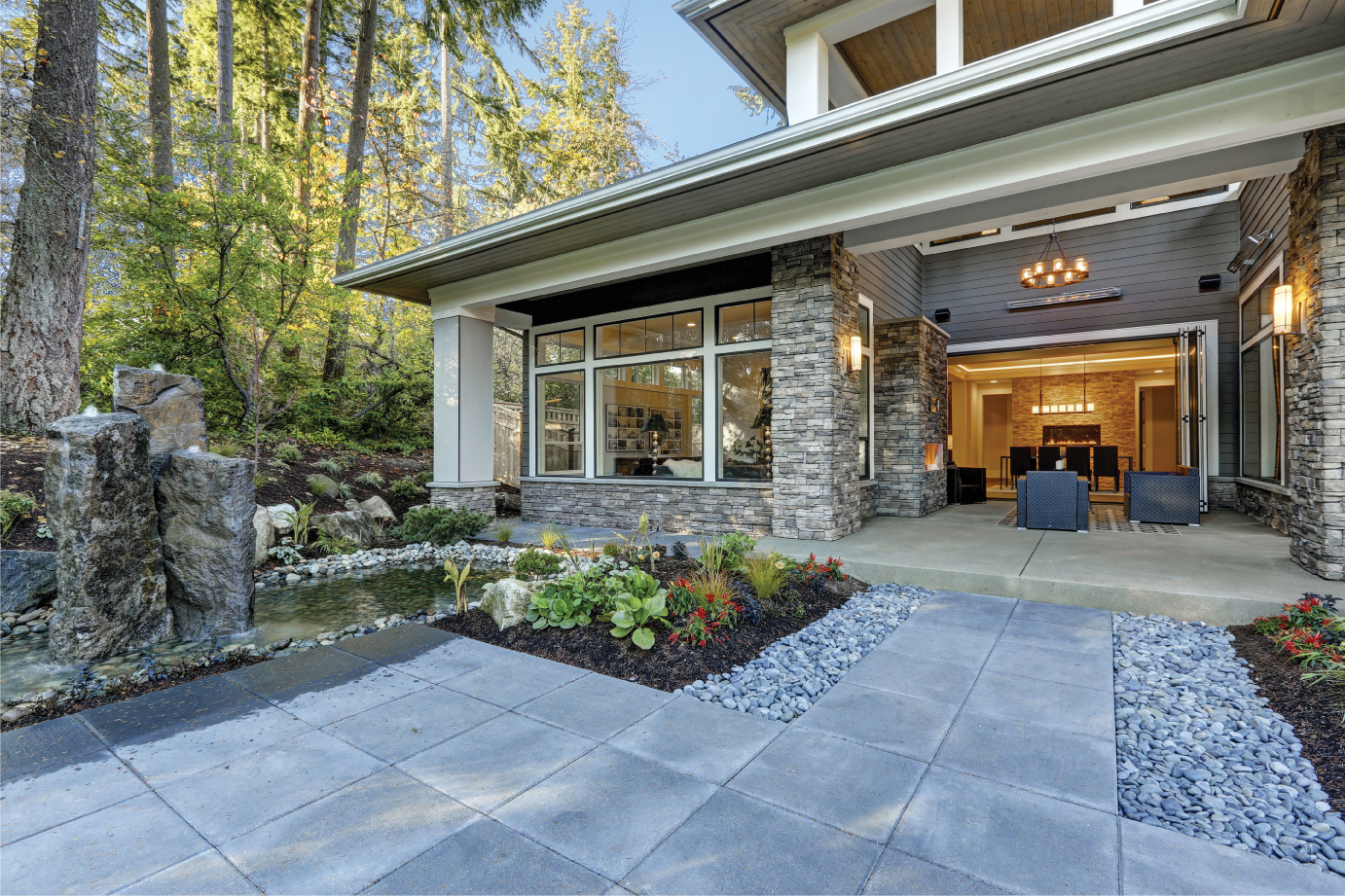 luxury home exterior featuring bluestone patio, stone veneer columns, and natural stone landscaping