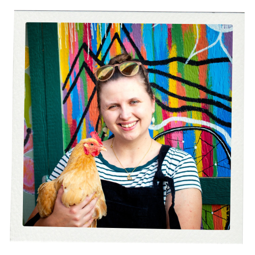 Caty Franco, a white woman with brown hair, holding a chicken in front of a colorful mural