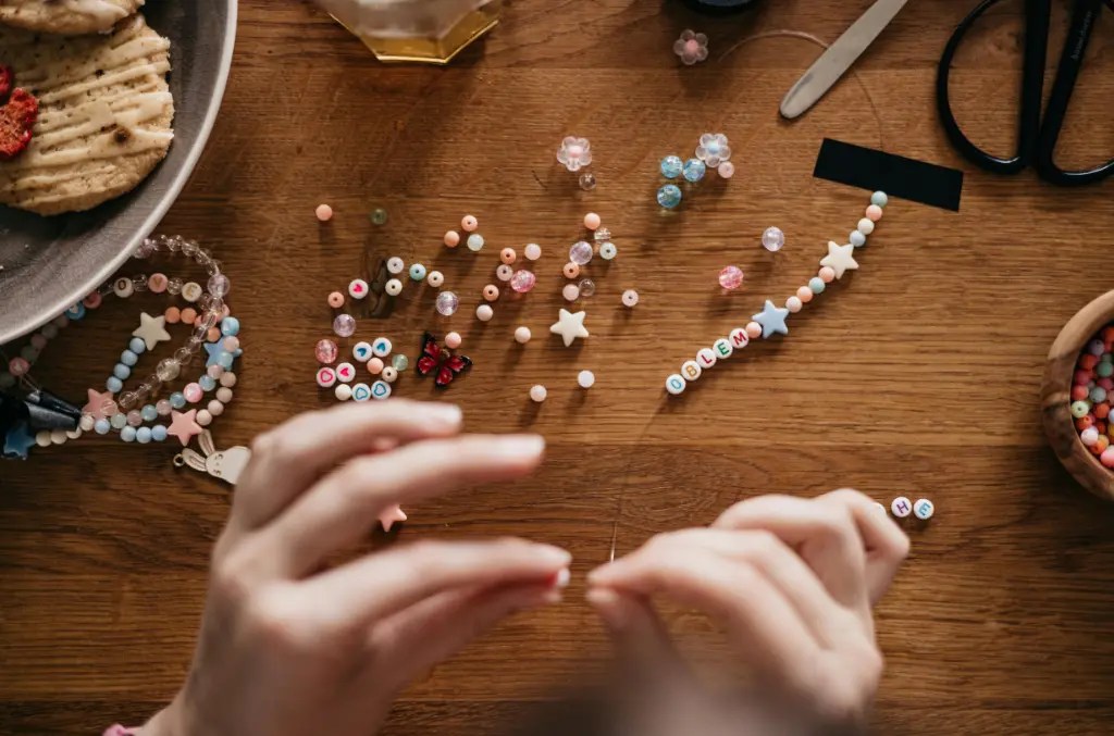 Ręce nawlekające kolorowe koraliki na nitkę – idealny przykład, jak zacząć robić biżuterię w domu krok po kroku