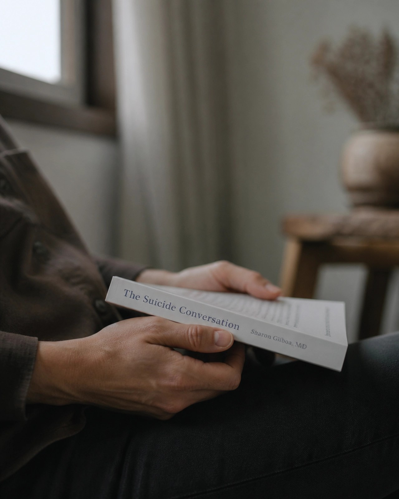 A close-up of hands holding a book titled The Suicide Conversation