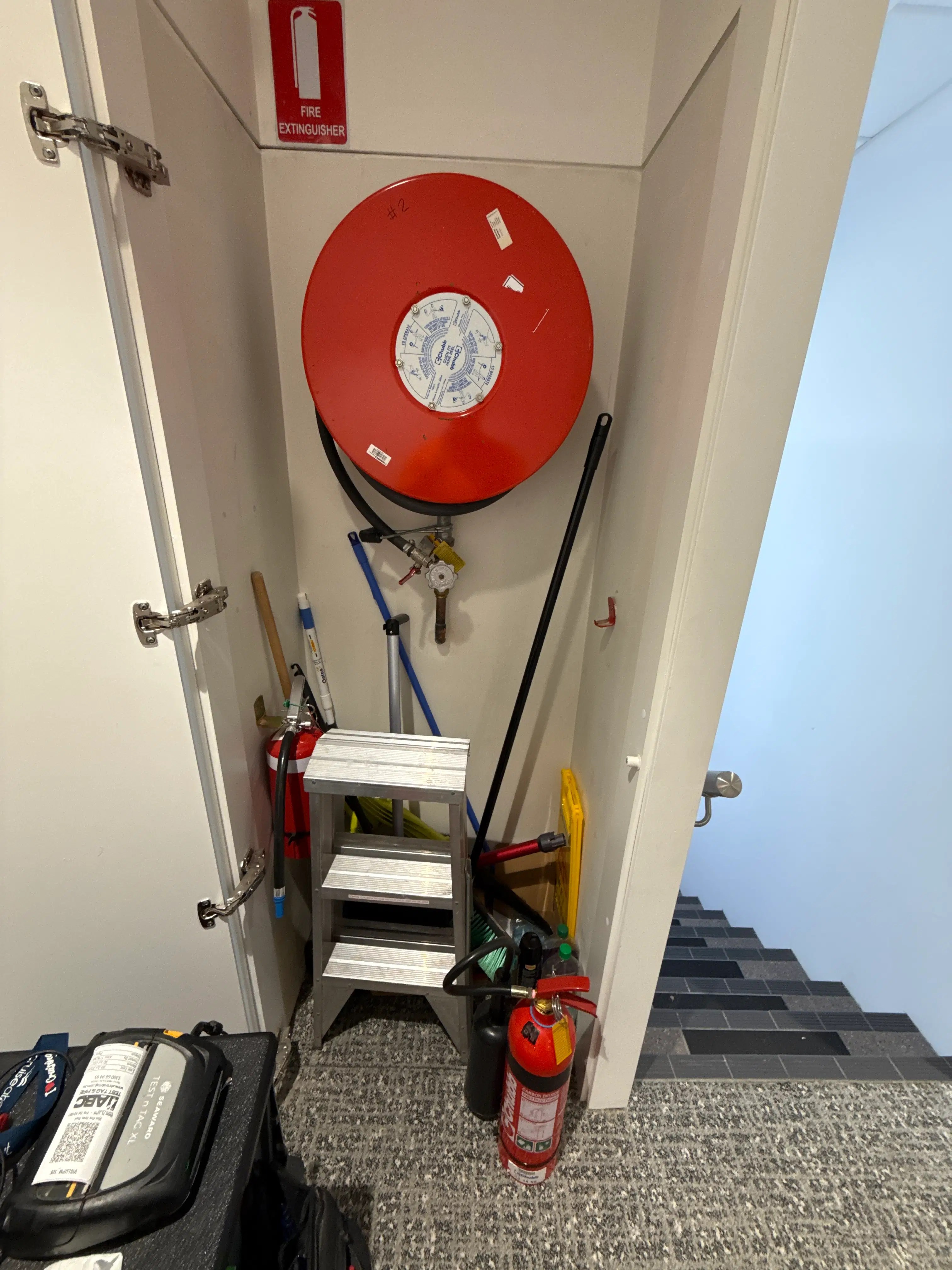 Fire extinguisher and fire hose reel equipment being inspected inside a workplace utility cupboard