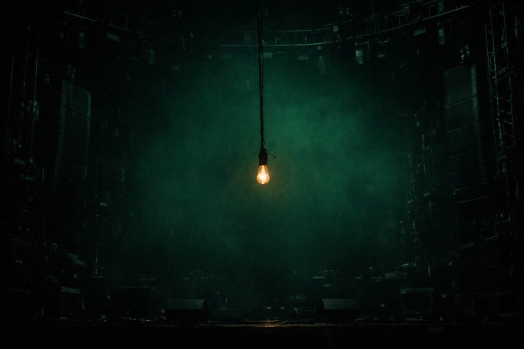 A dim light bulb on a massive darkened stage, illustrating underfunded growth and leadership gaps.