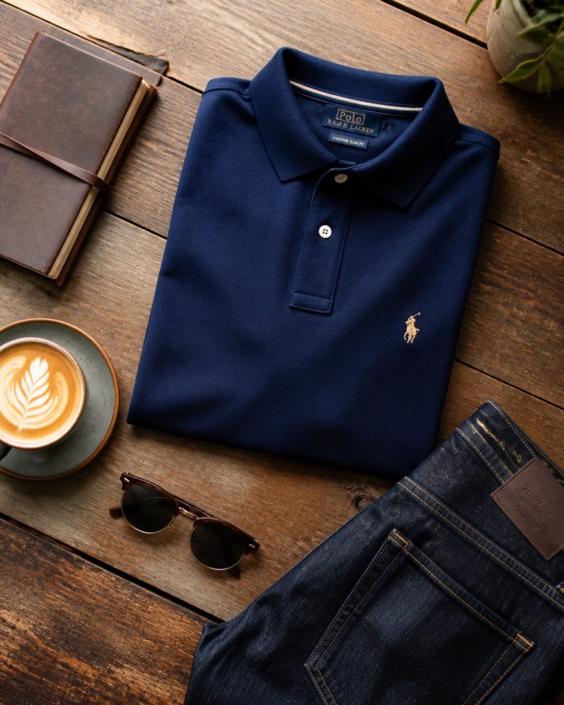 A flat lay of weekend essentials including a premium branded polo and denim