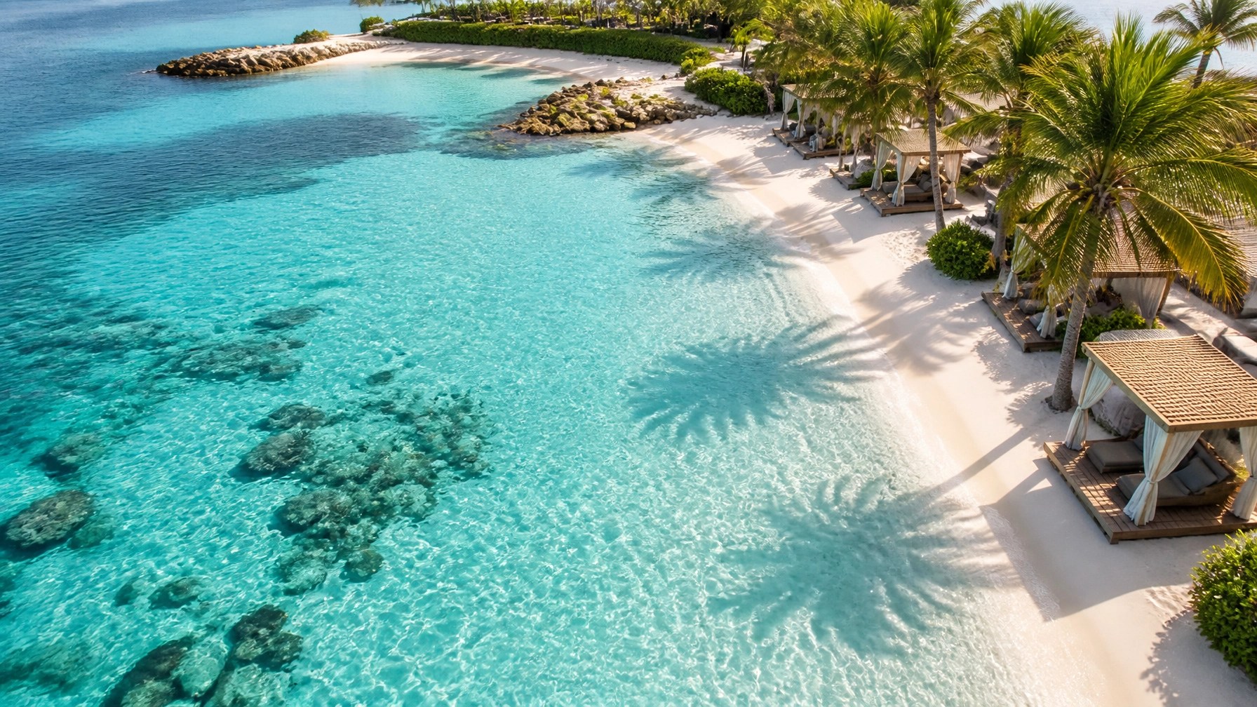 Aerial view of a pristine Bahamian private-island beach with turquoise water and empty cabanas