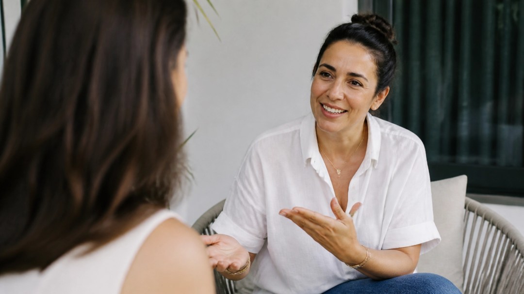 An approachable woman in her 40s sharing a candid, natural moment in a bright relaxed setting, reflecting real and supportive wellness coaching.