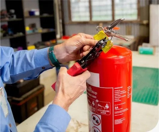 Technician attaching a compliance tag to a fire extinguisher during a routine inspection
