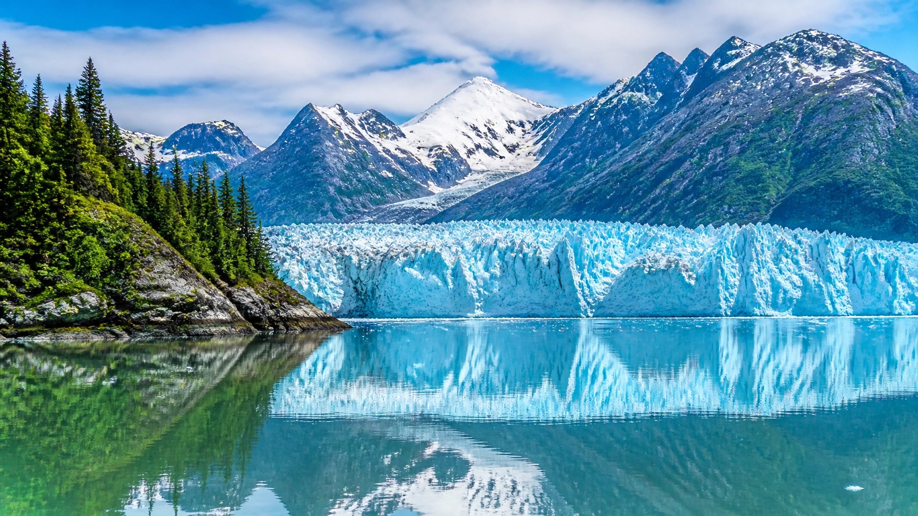 A serene, wide-angle landscape of Glacier Bay National Park in Alaska with crystal clear water.