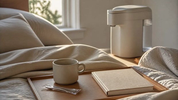 A compact neutral ramen cooker in a softly lit bedroom setting, with an empty mug waiting nearby