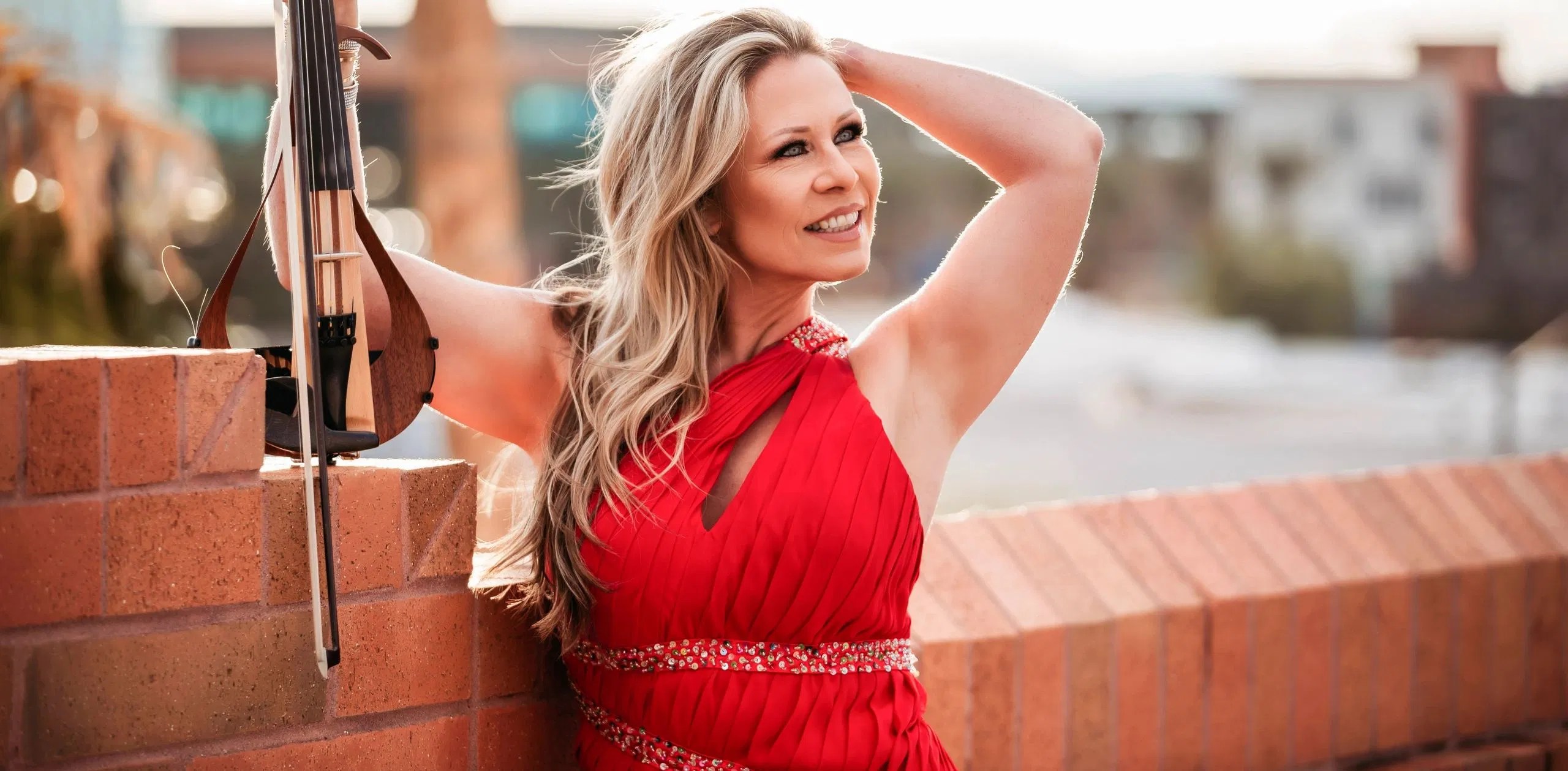 Carrie Caruso in a professional red dress with her electric violin outdoors.