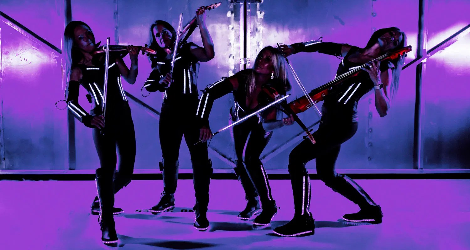 Urban Electra performing in futuristic outfits with vibrant purple lighting and high-energy stage presence
