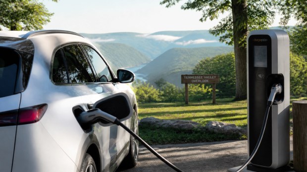 A modern electric vehicle charging at a sleek station with the lush, rolling green hills of the Tennessee Valley in the background.