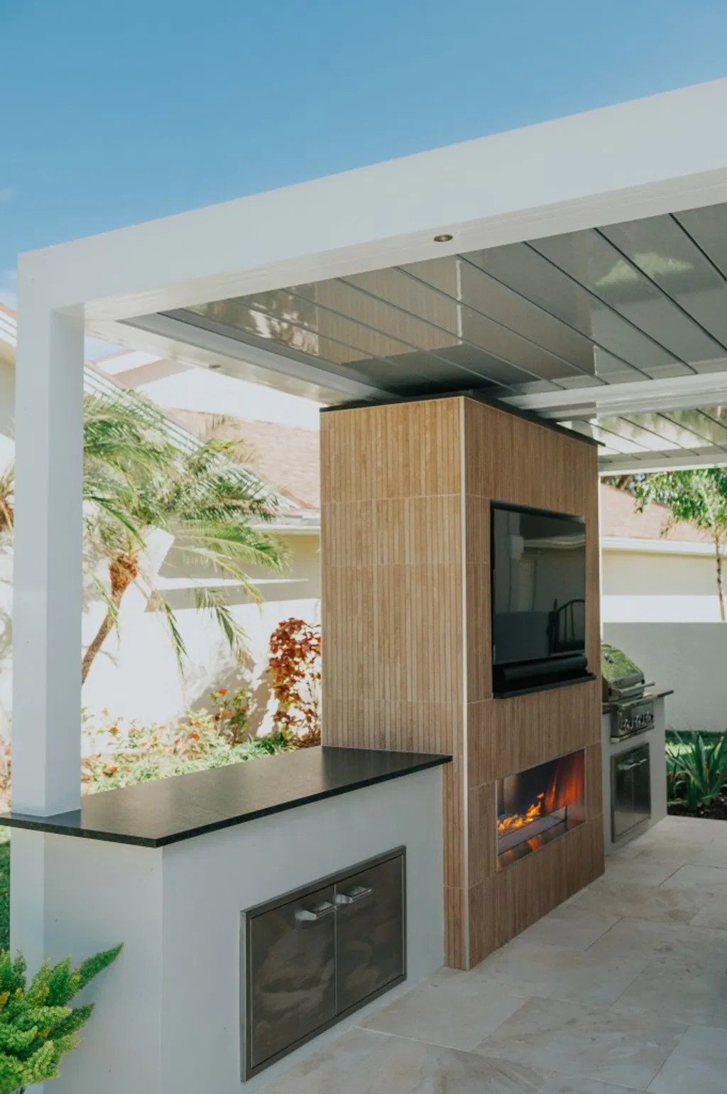 Modern outdoor living pavilion with an outdoor kitchen, bar, fireplace, and television