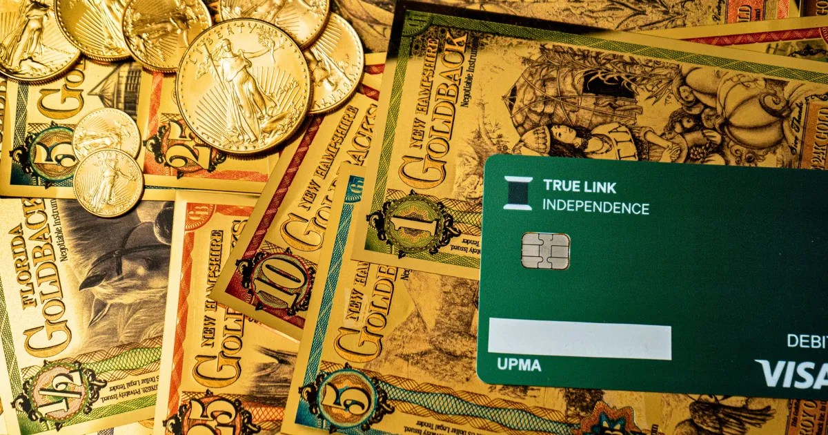 Goldbacks, gold coins, and a debit card displayed together, illustrating the bridge between physical metals and digital payments.