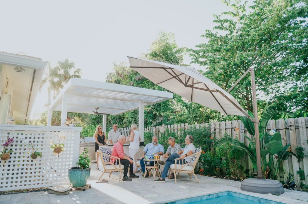 Friends enjoying a social gathering under a custom louvered pergola by the pool.