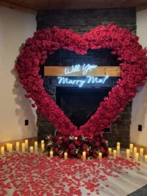 A romantic cabin fireplace setup with a red rose arch, candles on the floor, and a 