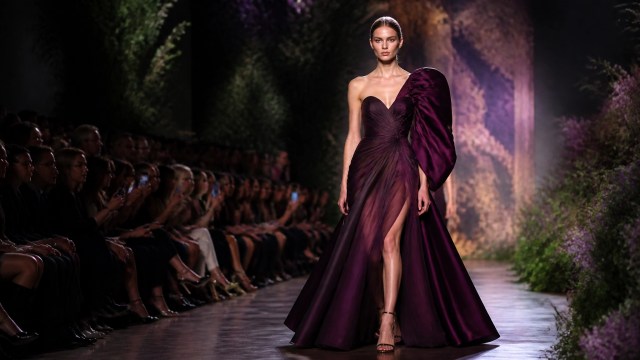 A dramatic evening couture look appears on the runway under sharp editorial lighting during fashion week