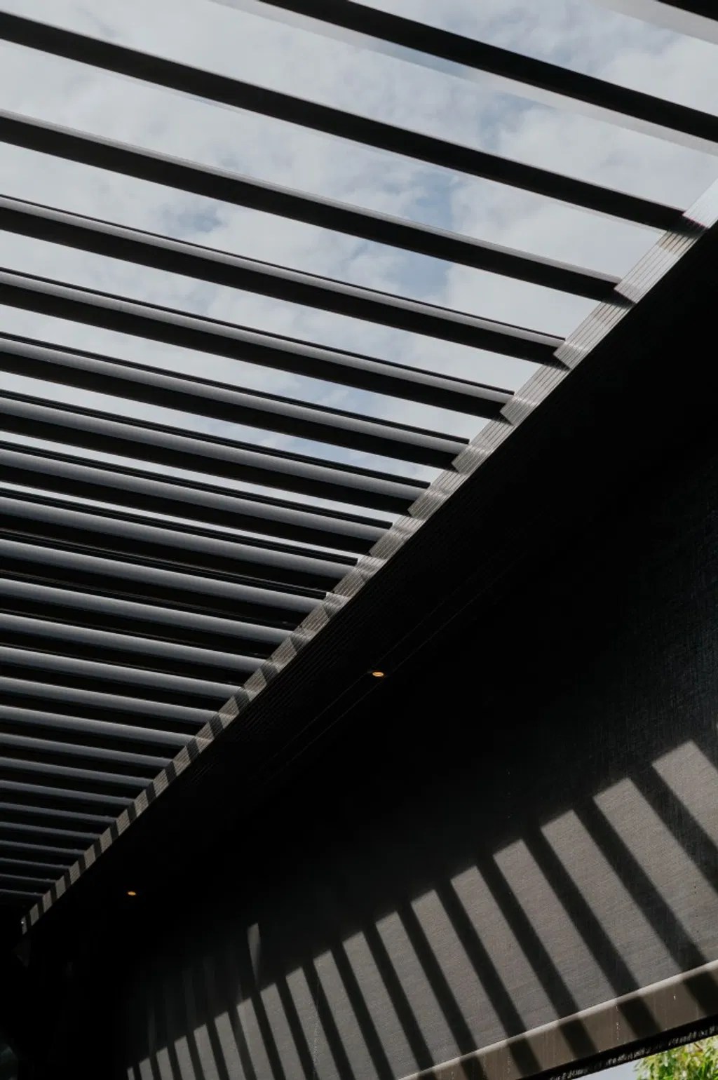 A modern motorized louvered roof system in a partially open position, showing how precision louvers allow for customizable sunlight and airflow.