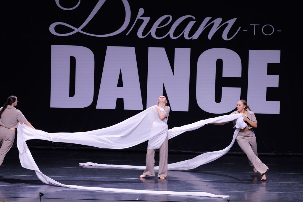 Three company-level dancers perform a contemporary routine on stage with long white fabric props