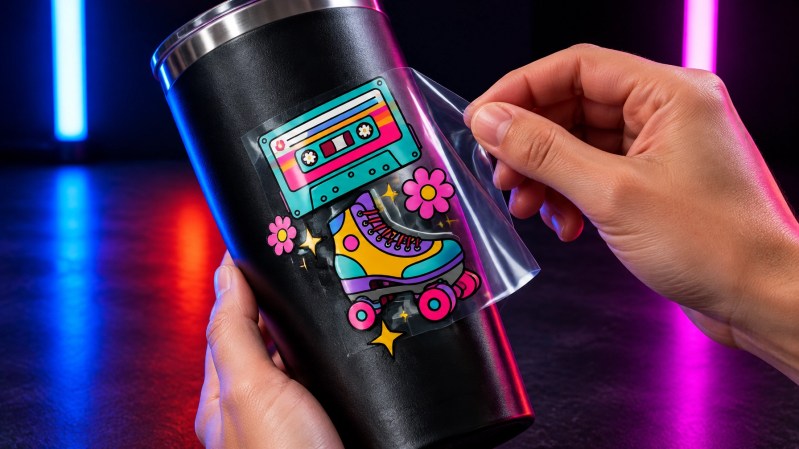 UV DTF transfers for tumblers being applied to a matte black tumbler under dramatic studio lighting