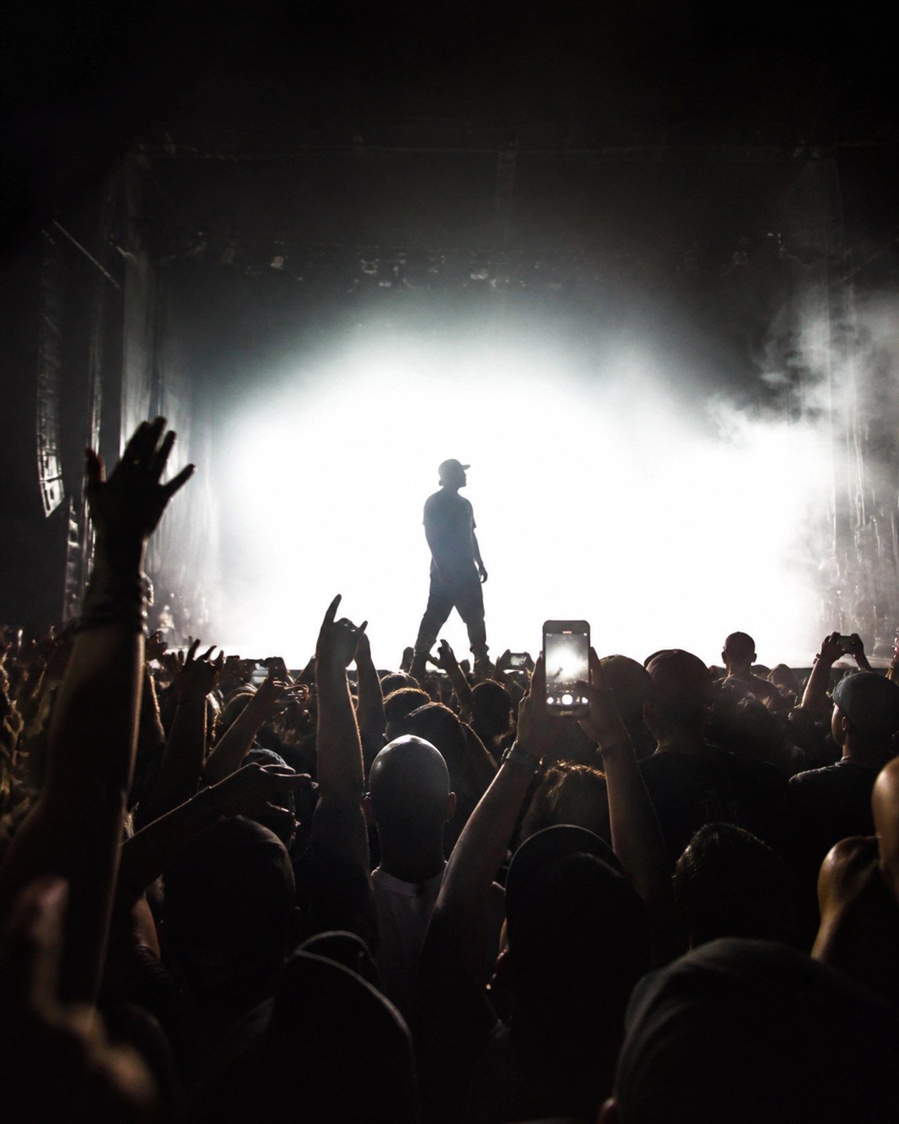 Silhouette of a performer against a bright stage light at Yankee Stadium with a sea of hands raised