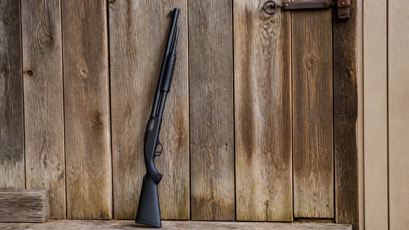 A realistic, professional photo of a budget-friendly pump-action shotgun leaning against a rustic wooden wall.