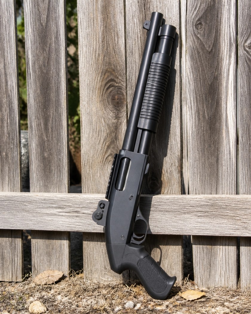 Modern tactical pump-action shotgun with a pistol grip leaning against a wooden fence.
