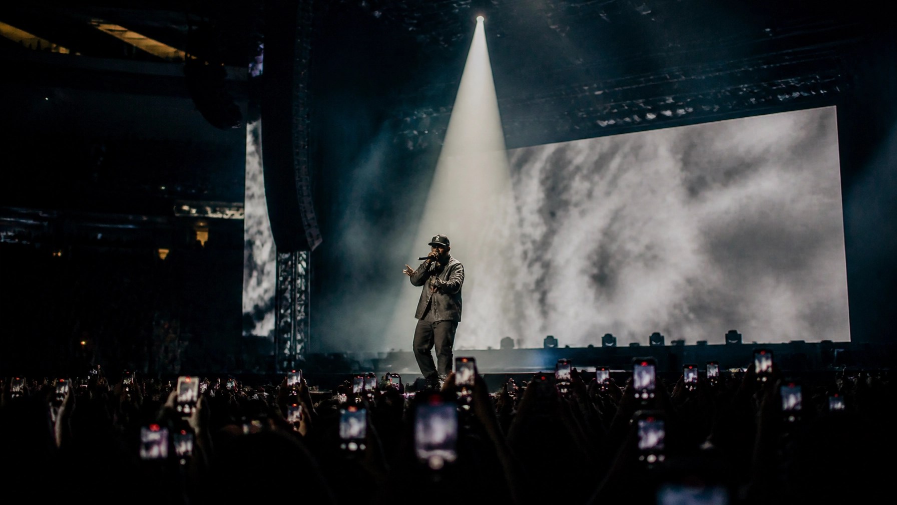 A solo hip-hop artist performing on a massive arena stage with dramatic lighting