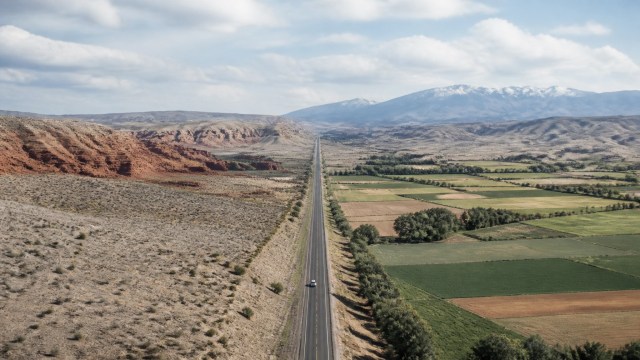 A long road gradually transitioning through desert, canyon, farmland, and mountain landscapes