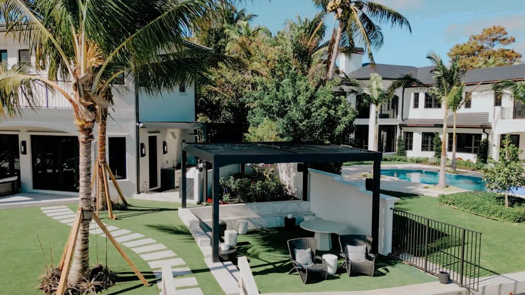 A modern South Florida backyard with a black motorized pergola, pool, lounge area, and tropical landscaping