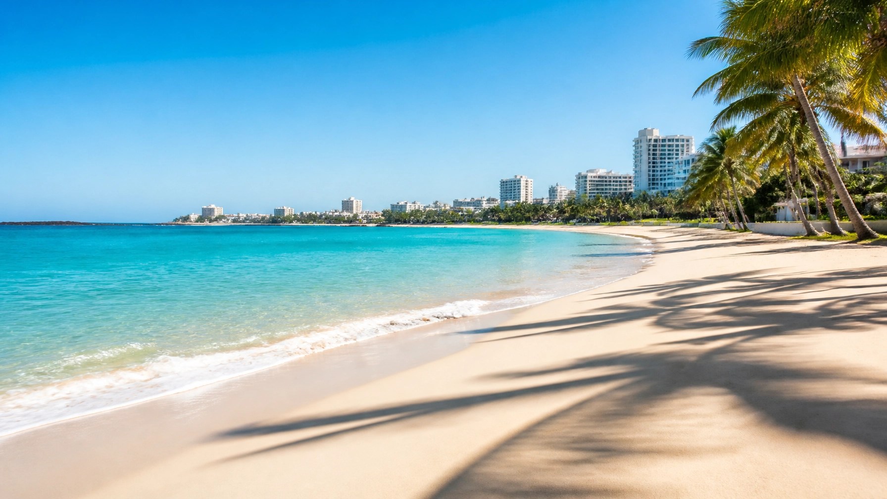 Pristine Condado Beach in San Juan with aquamarine water, silky white sand, palm shadows, and a refined resort skyline in the distance
