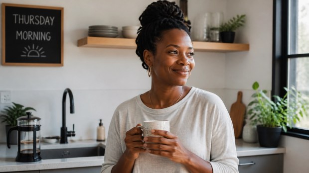 A Black woman smiling peacefully in a sunlit modern kitchen, enjoying a morning cup of artisan coffee