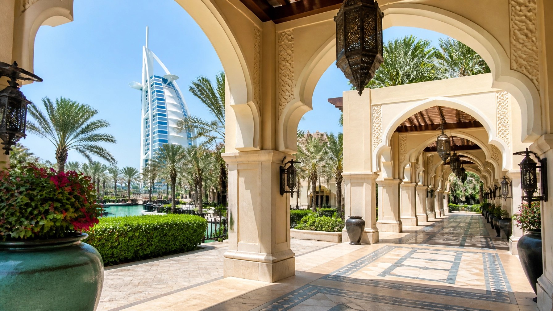 Bright daytime Arabian archway and shaded walkway detail at Madinat Jumeirah with ivory arches, greenery and Burj Al Arab beyond