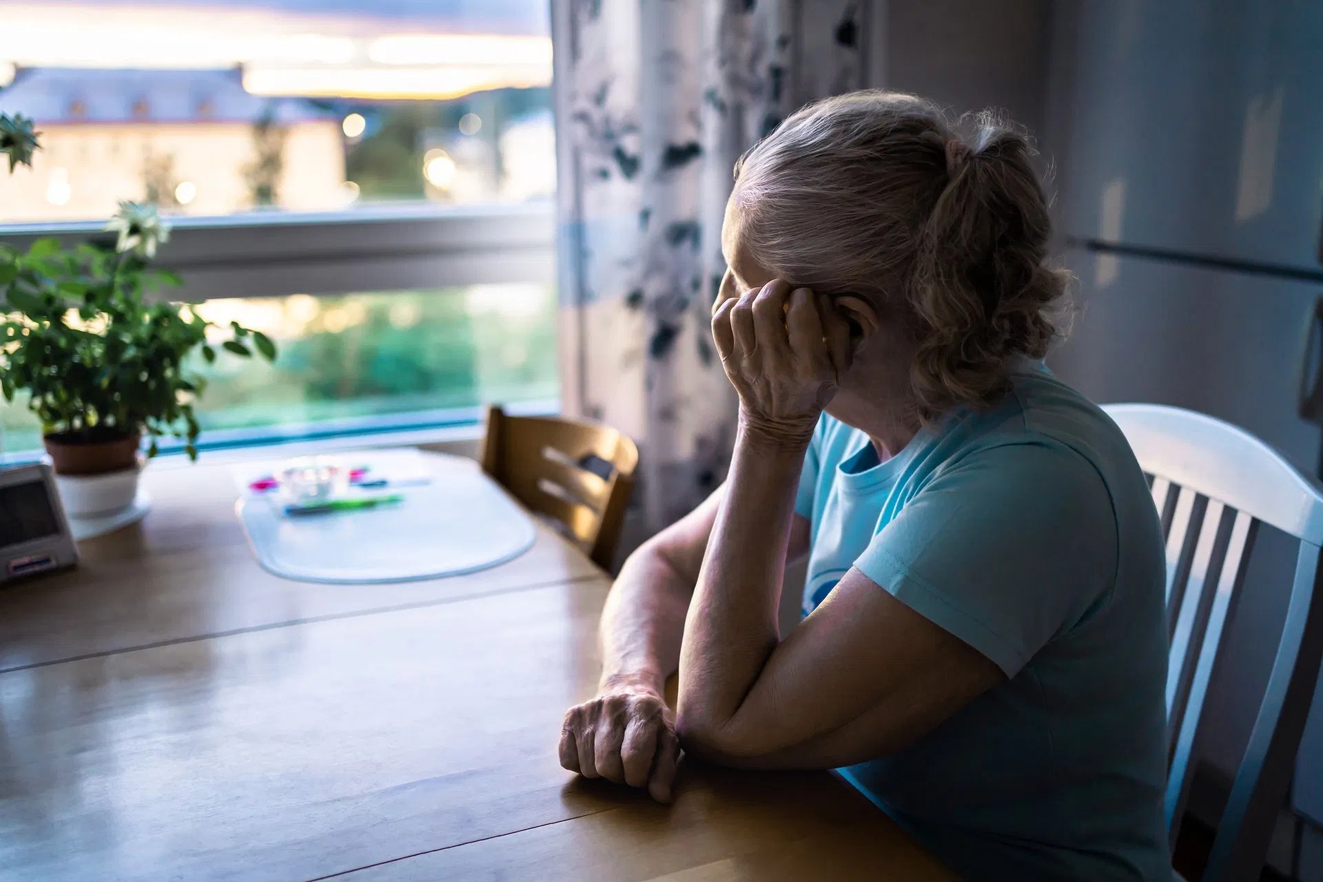 A woman sitting alone at a dining table and looking toward a window