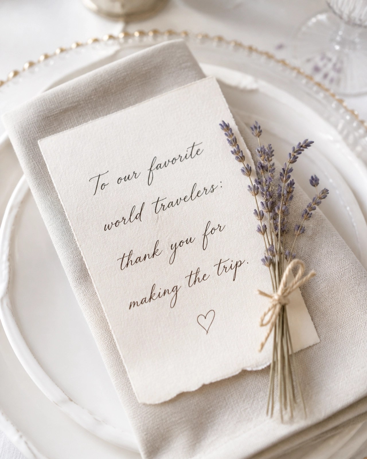 A close-up shot of a beautiful wedding table setting with a card that says 'To our favorite world travelers: thank you for making the trip.' next to a sprig of dried lavender.