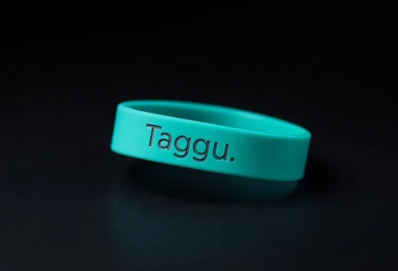 A close-up of a teal Taggu wristband against a dark background