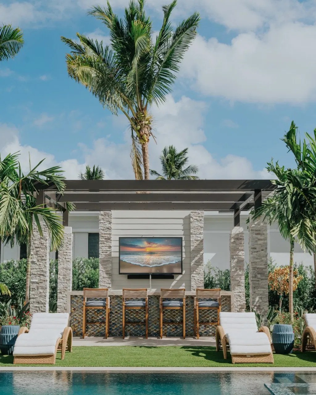 A custom louvered roof pergola with stone pillars and a poolside lounge, showcasing the seamless integration of a high-end structure into a luxury backyard entertainment space.