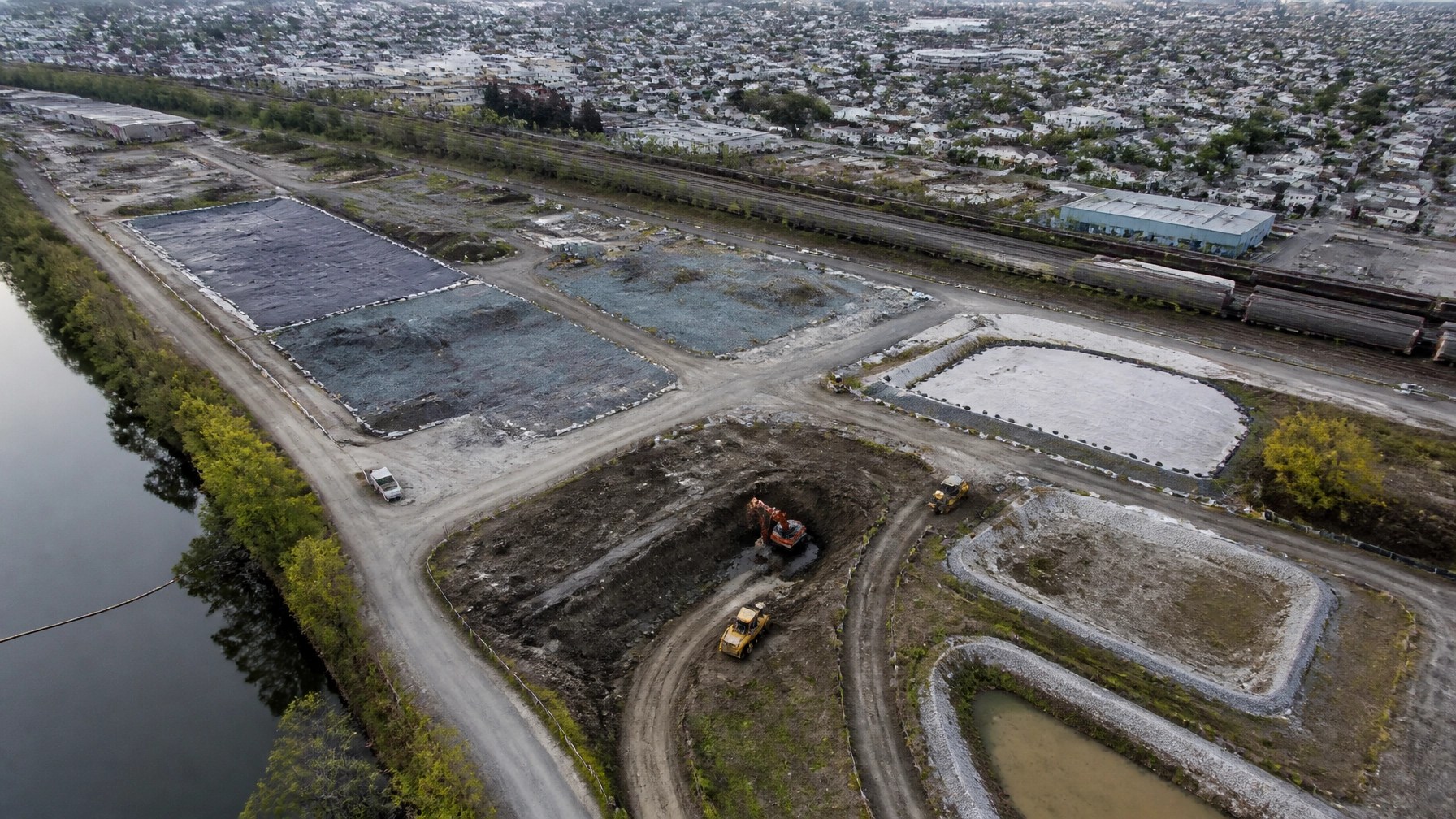 Aerial view of a New Jersey industrial redevelopment site showing excavation zones, capped areas, monitoring wells, and nearby freight infrastructure