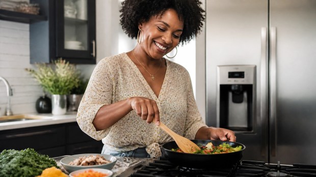 A Black woman cooking a healthy, savory meal in a bright, beautiful home kitchen, tossing fresh ingredients in a skillet