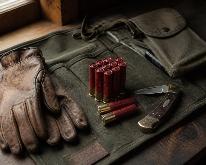 Survival hunting kit featuring .410 slug shells, leather gloves, and a folding knife on canvas.