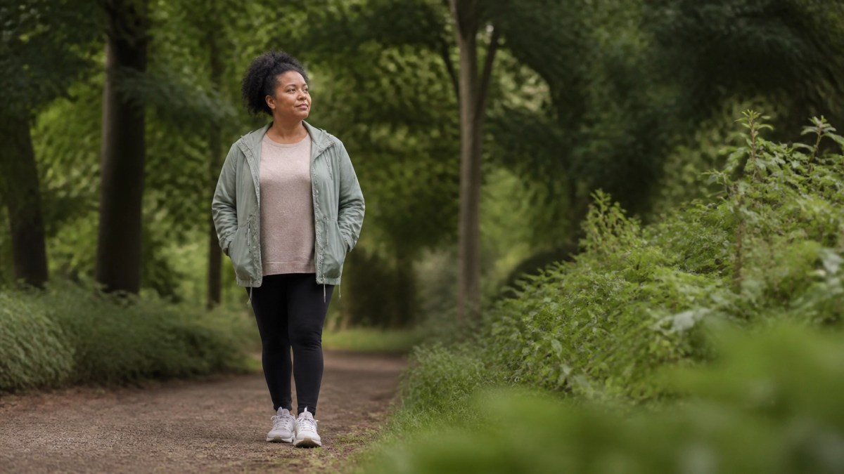 An adult person of color walking peacefully through a lush green park, captured in a natural, candid style with soft daylight and a serene, reflective mood.