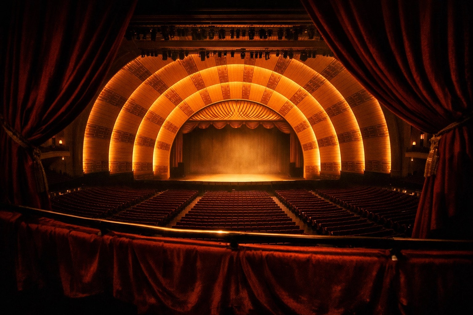 View from the mezzanine of Radio City Music Hall's glowing golden proscenium arches and empty theater seating.