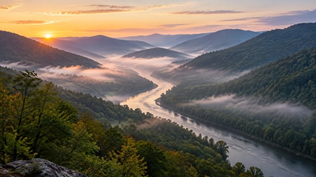 A misty mountain valley with a river at first light and forested ridgelines