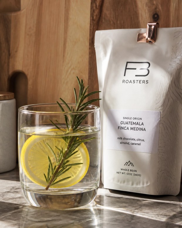 A close-up of the lemon water and rosemary ritual foundation next to FB Roasters coffee.