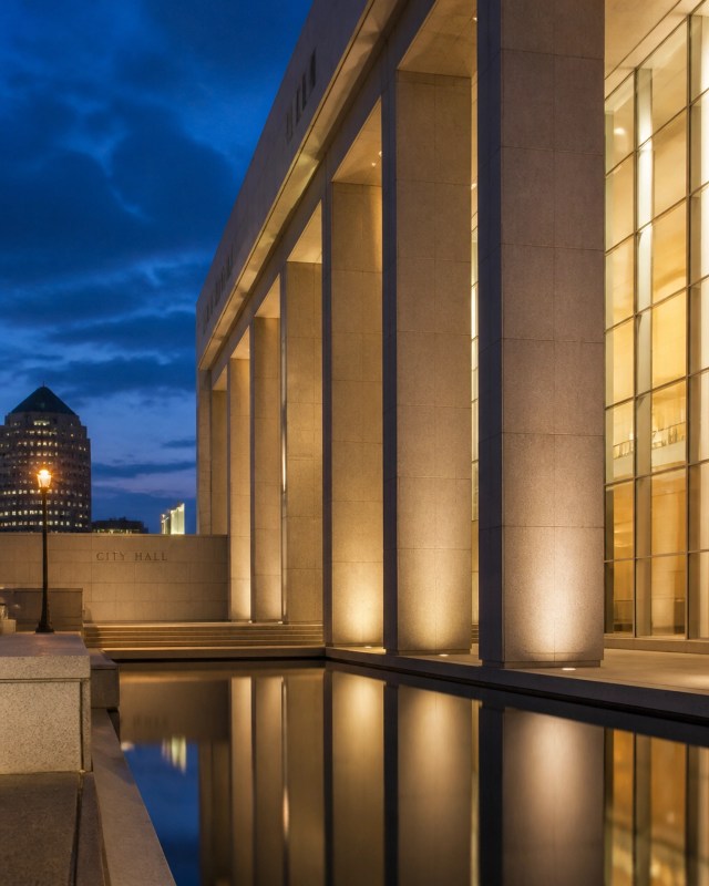 A cinematic dusk view of a modern government plaza featuring clean architectural lines and glowing interior lights.