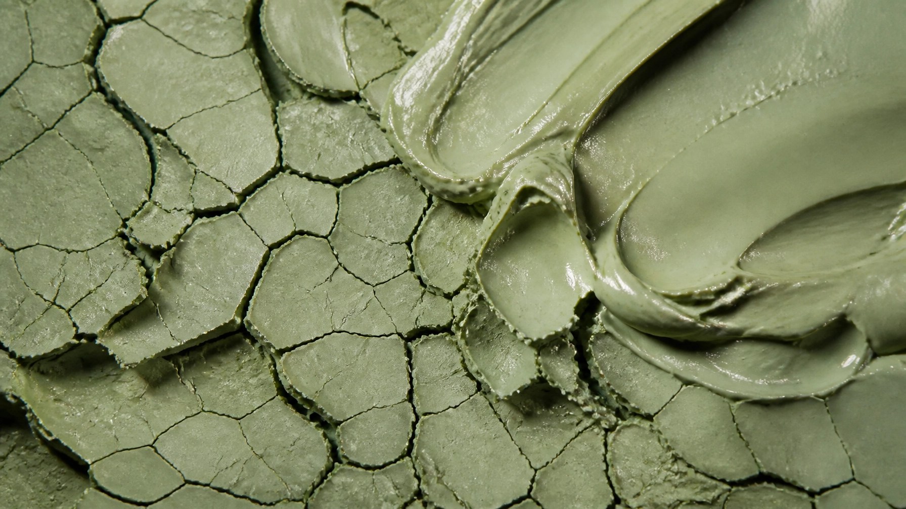 An abstract, high-detail macro shot of dried green clay texture.