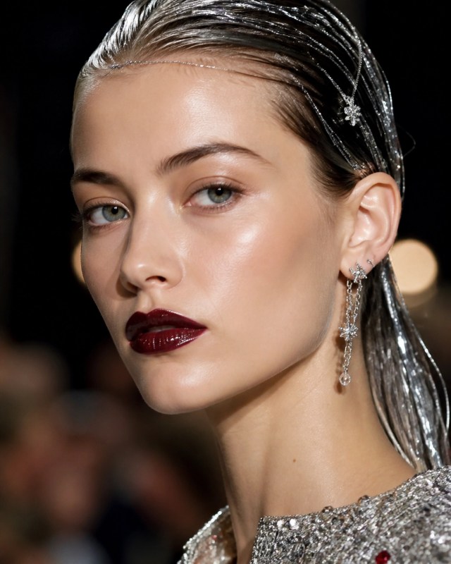 Runway beauty portrait with luminous skin, softly blurred metallic garnet lips, slicked-back hair, silver tinsel, and delicate hair jewelry