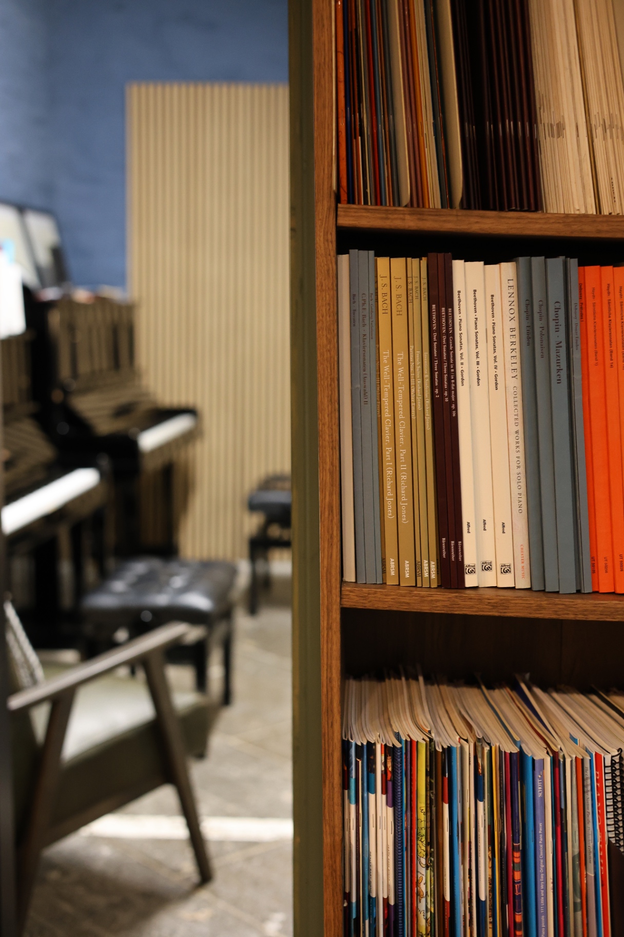 AberMusic Studio Bookshelf Bookshelf filled with sheet music editions and music theory books in the AberMusic Studio; upright pianos and seating visible in the background, creating an organised and inspiring learning environment for piano and music theory lessons.
