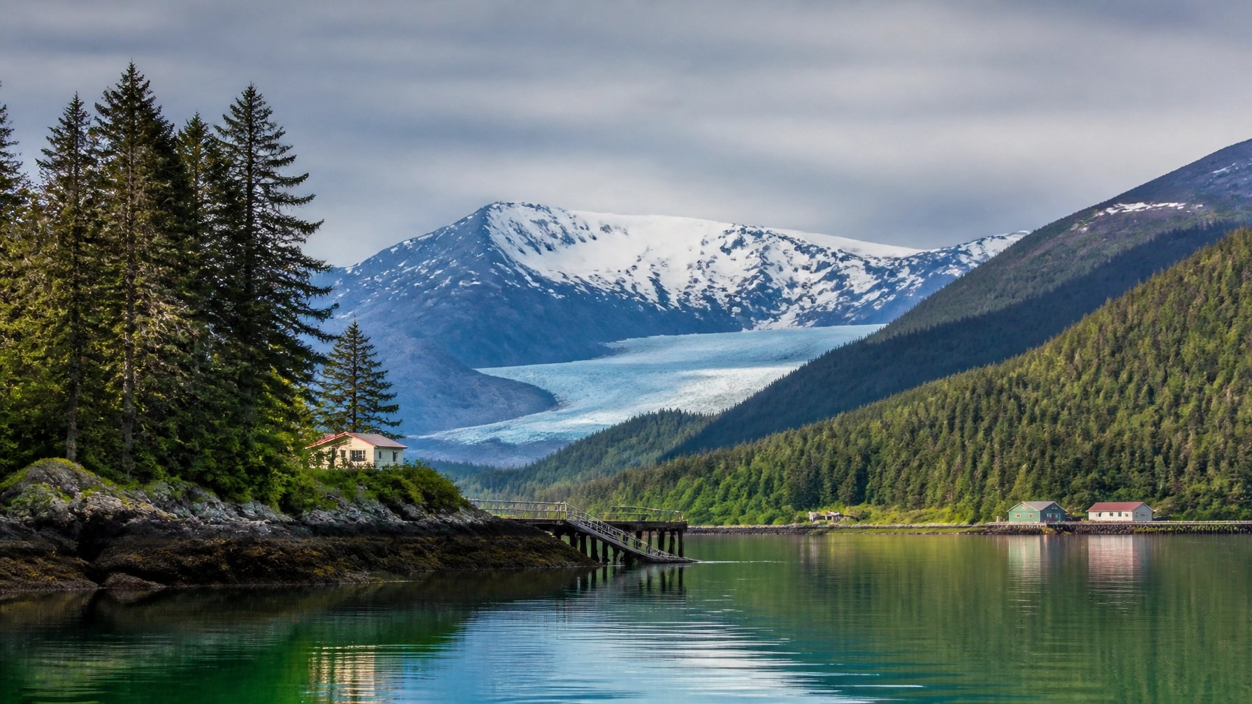 A scenic view of Juneau’s harbor, forested shoreline, snow-capped mountains, and distant blue glacier